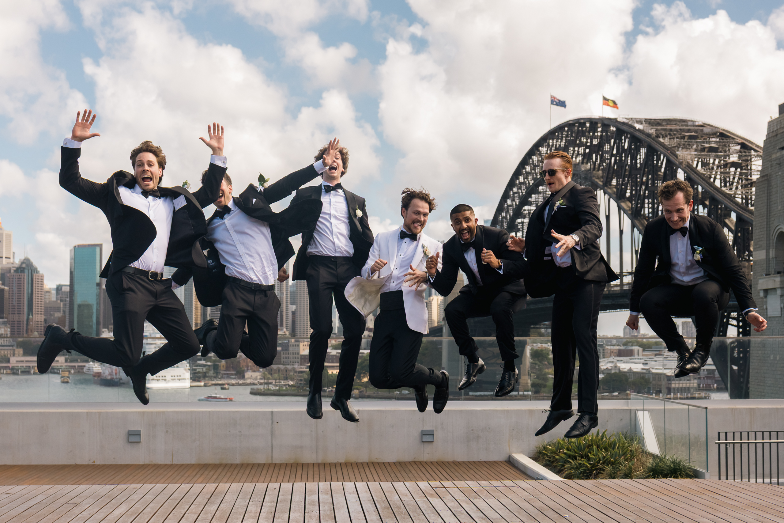 Happy groomsmen jumping with the Sydney Harbour Bridge in the background before the wedding.